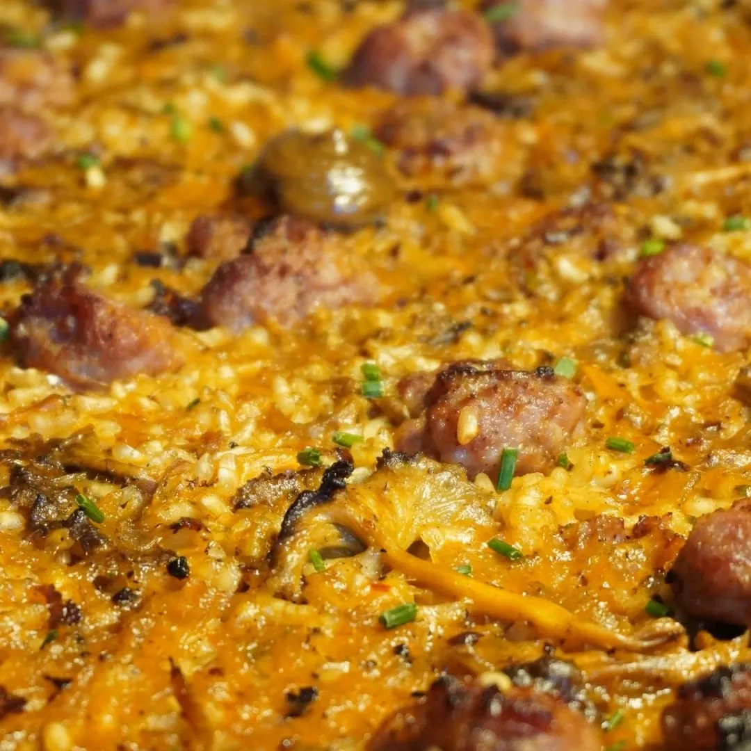Un arròs de muntanya vist de prop dins la paella, amb talls de botifarra i bolets repartits per sobre.
