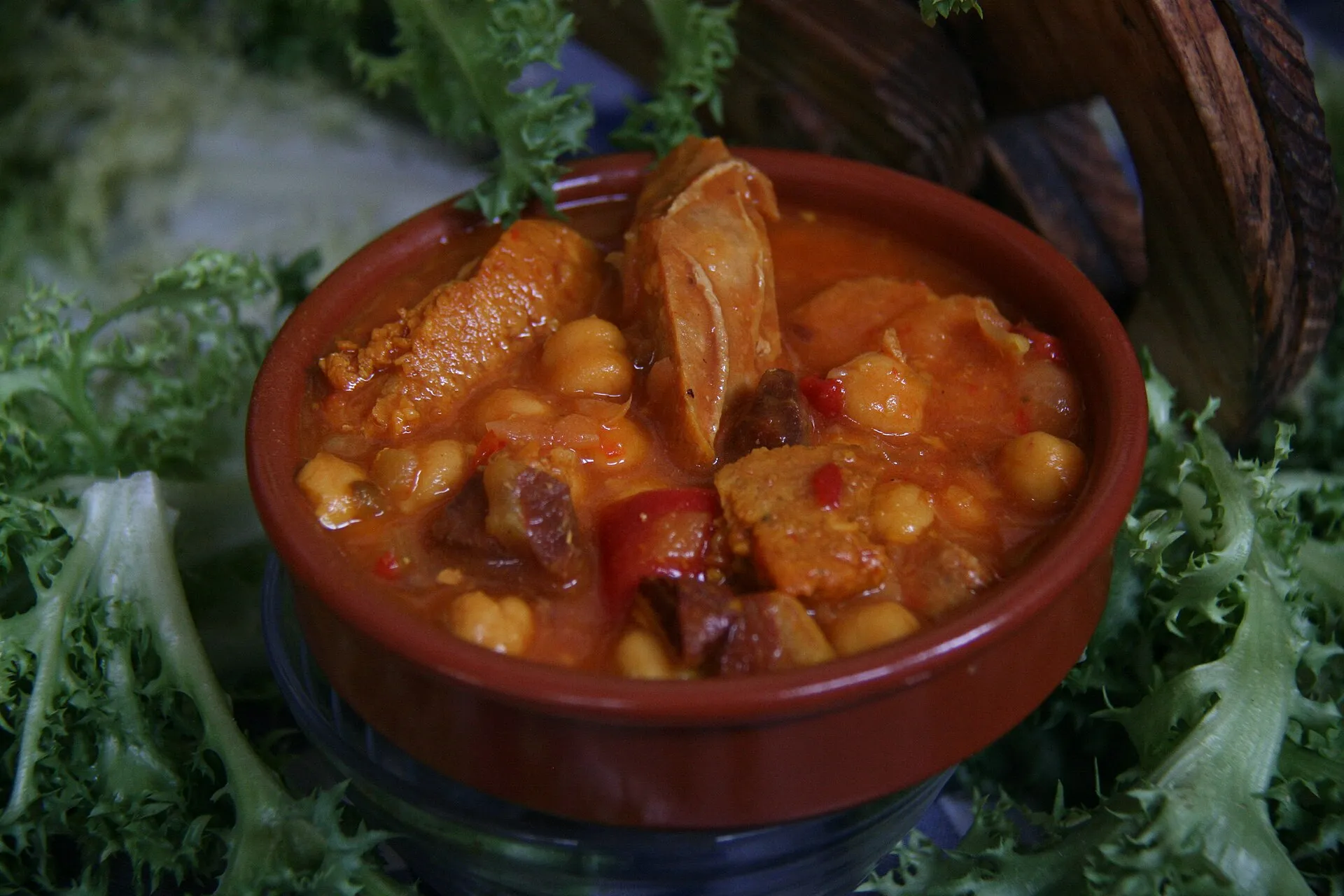 Una cassola de fang plena de cigrons guisats amb botifarra, cansalada i talls de pebrot vermell, coberts d’un brou espès de tomàquet.