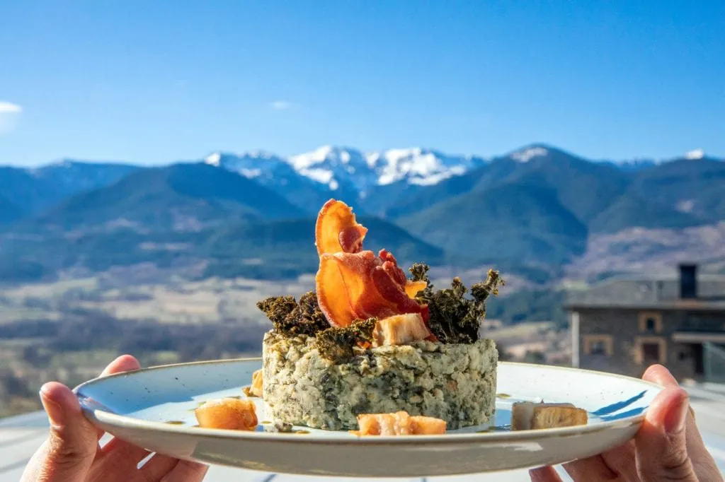 Un trinxat de la Cerdanya servit en timbal, amb kale cruixent i un tall de cansalada torrada al damunt, sostingut a pols davant del pla de la vall i les carenes nevades.